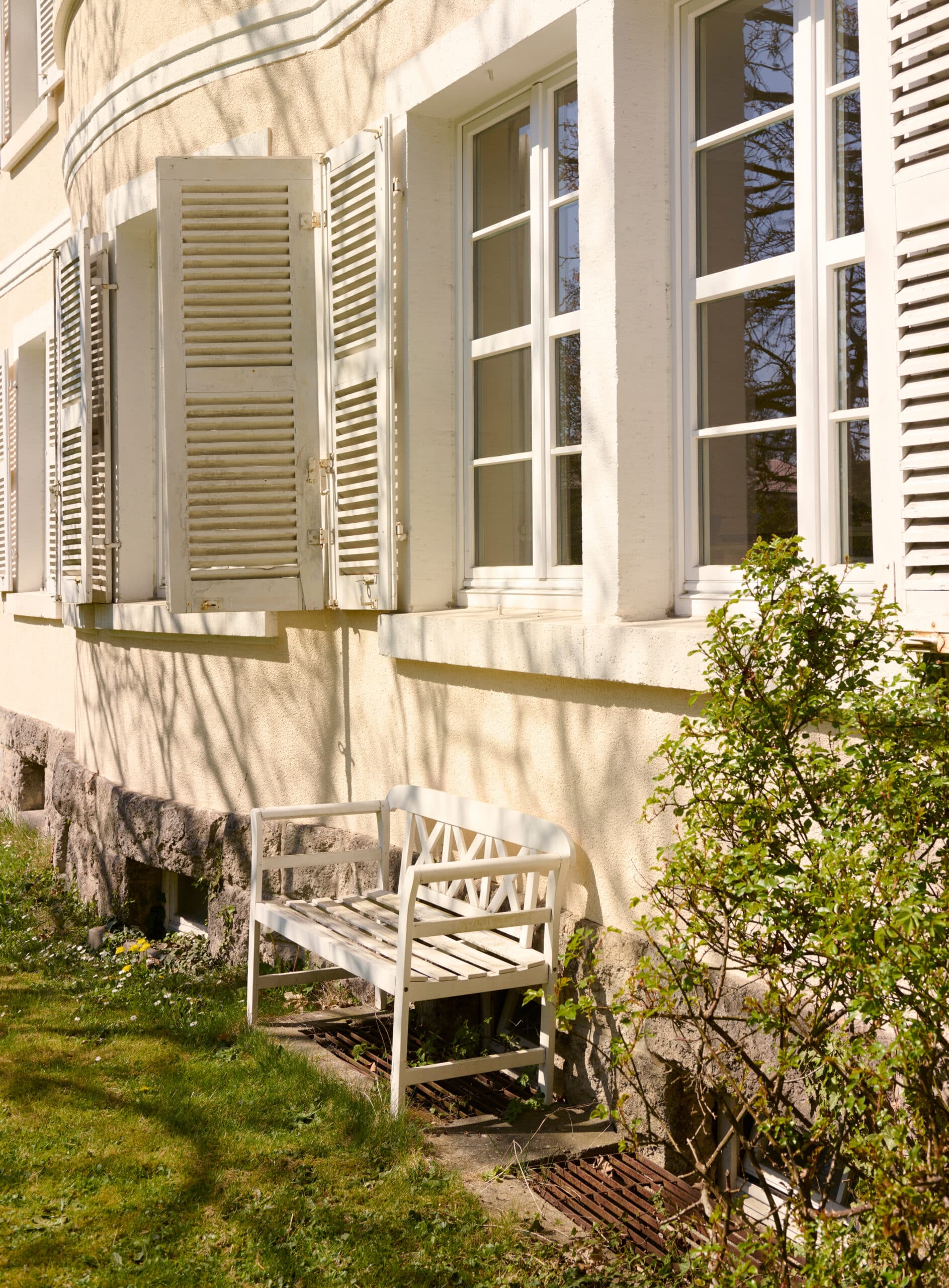 Außenansicht des Praxisgebäudes von Dr. Ratjen und Dr. Orth-Tannenberg mit weißen Fensterläden und Gartenbank.