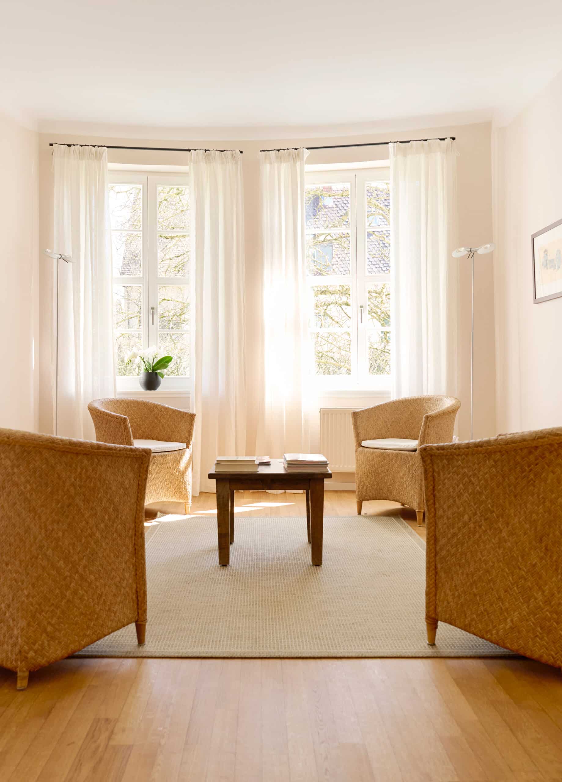 Helles, freundliches Wartezimmer mit vier Korbsesseln, Holztisch und großen Fenstern in der Praxis Dr. Ratjen und Dr. Orth-Tannenberg in Königstein.